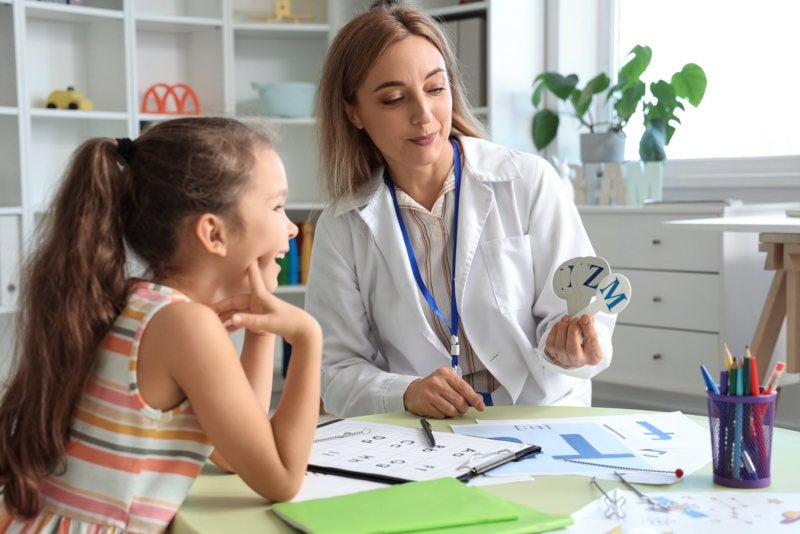 A female SLP showing letter cues to a young patient