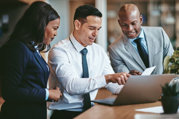 Diverse trio of business professionals reviewing documents on a laptop