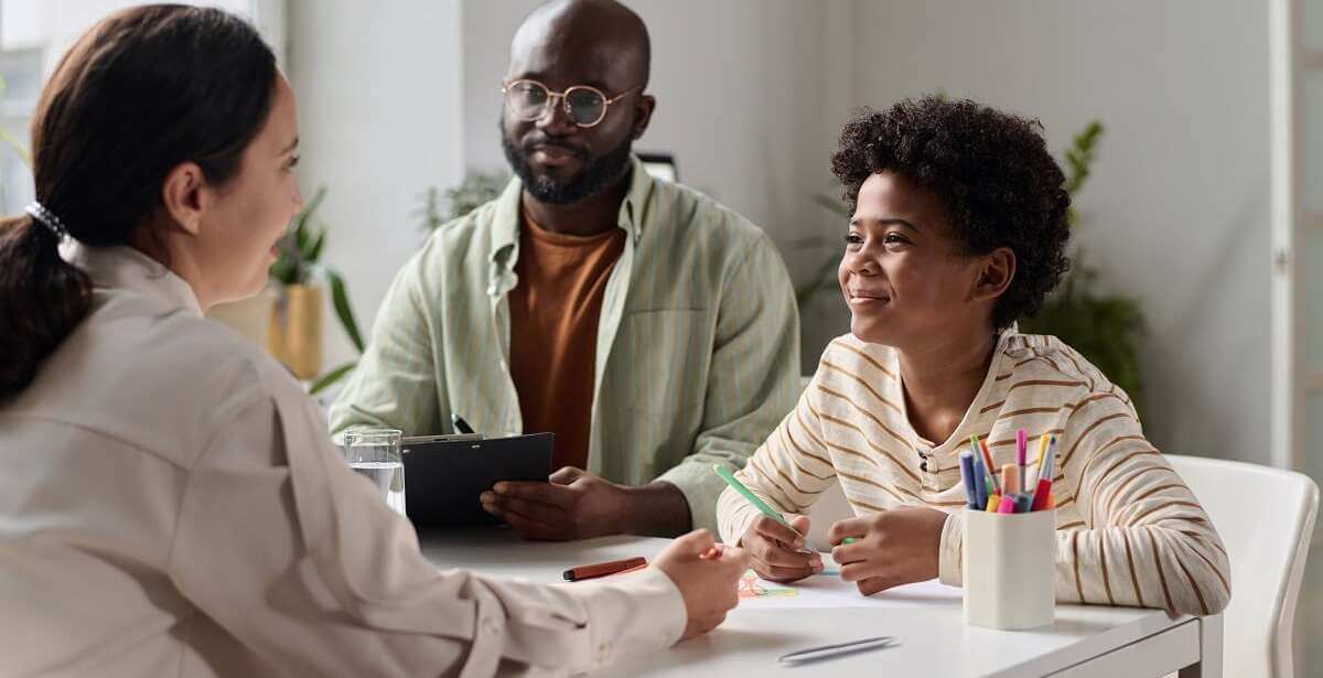 A smiling young boy talking to a friendly social worker at a desk in the office