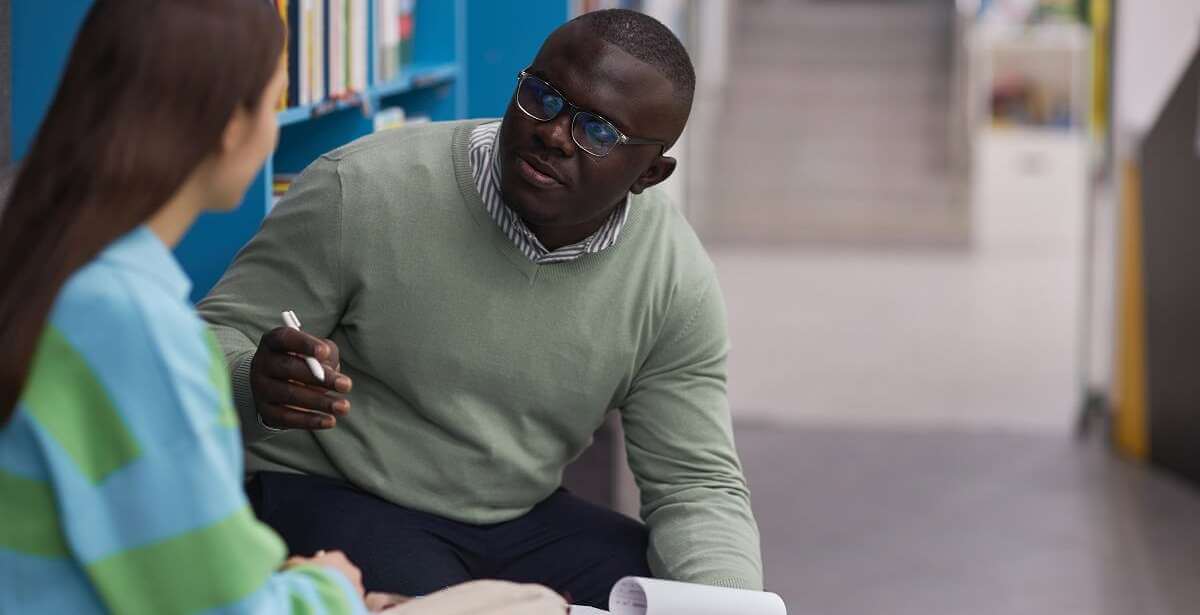 A school counselor talks with a student in a school library.