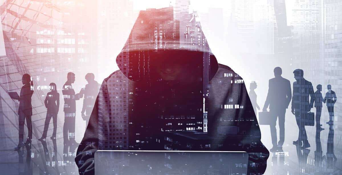Hacker in a hoodie against a background of shadowy figures