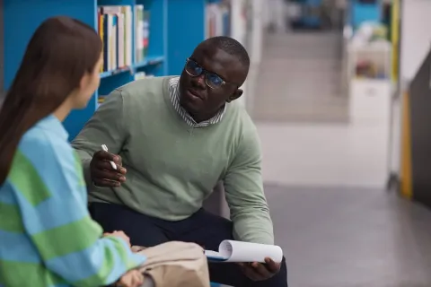 A school counselor talks with a student in a school library.